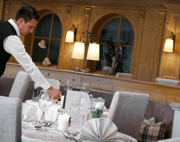 Ein Kellner richtet in einem holzgetäfelten Restaurant einen Tisch mit weißen Servietten und Gläsern her.